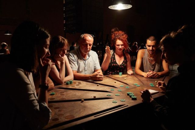 Spectateurs autour des tables de jeu de £¥€$ d’Ontroerend Goed